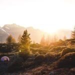 Tente de camping rose installée dans un paysage montagneux boisé au coucher de soleil