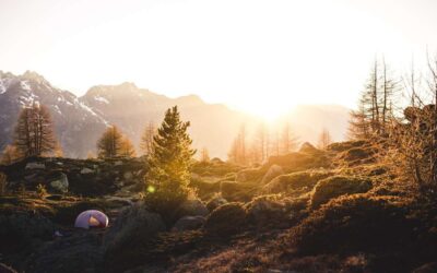 Tente de camping rose installée dans un paysage montagneux boisé au coucher de soleil