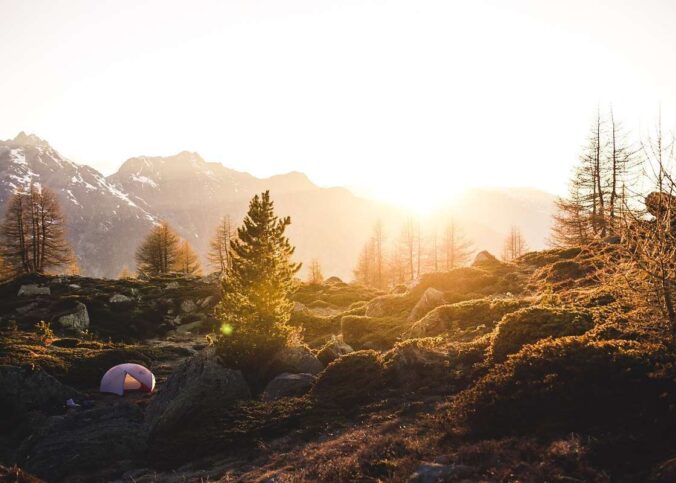Tente de camping rose installée dans un paysage montagneux boisé au coucher de soleil