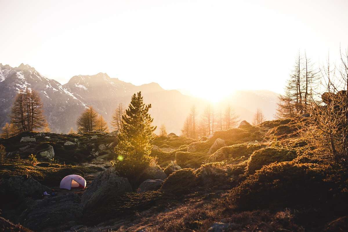 Tente de camping rose installée dans un paysage montagneux boisé au coucher de soleil