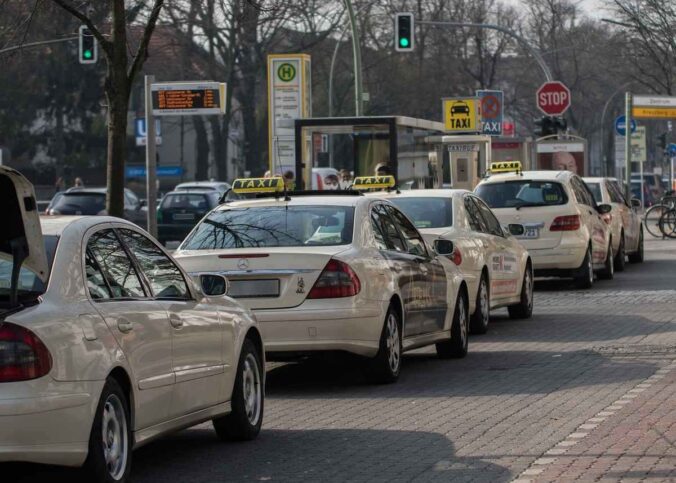 File de taxis blancs garés à une station avec leurs toits illuminés, arbres nus en arrière-plan