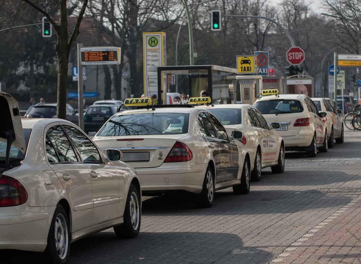 File de taxis blancs garés à une station avec leurs toits illuminés, arbres nus en arrière-plan