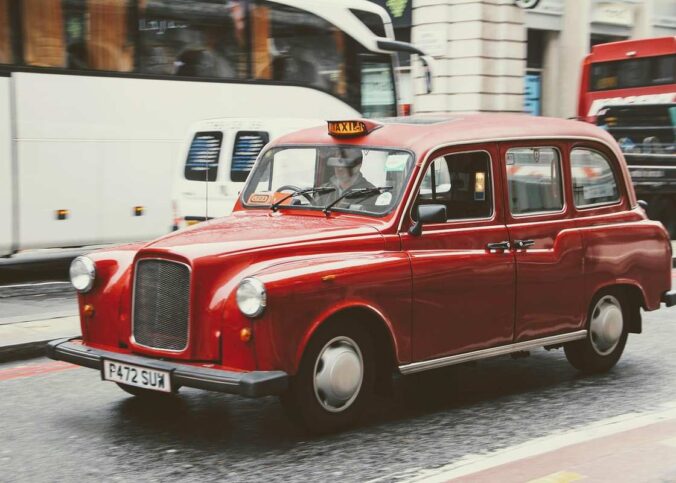 Taxi londonien rouge circulant en rue urbaine avec plaque de taxi éclairée
