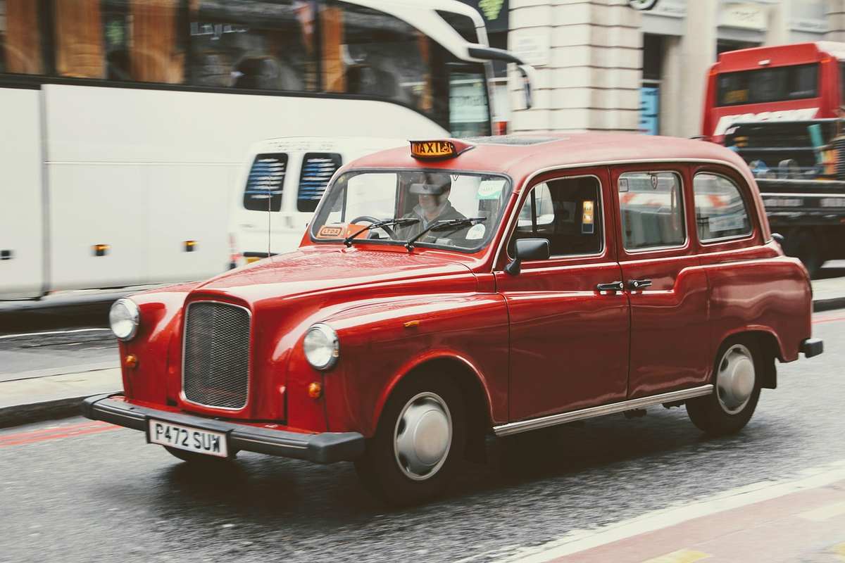 Taxi londonien rouge circulant en rue urbaine avec plaque de taxi éclairée