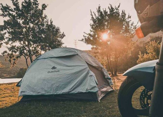 Tente de camping blanche près d'un lac, soleil couchant, moto à l'avant-plan
