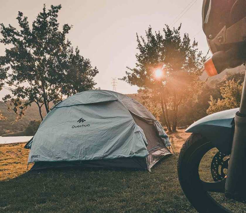 Tente de camping blanche près d'un lac, soleil couchant, moto à l'avant-plan