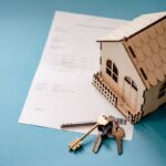 Une petite maison en bois, un document et des clés sur fond bleu