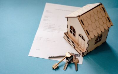 Une petite maison en bois, un document et des clés sur fond bleu
