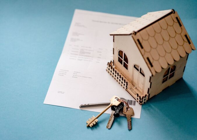 Une petite maison en bois, un document et des clés sur fond bleu