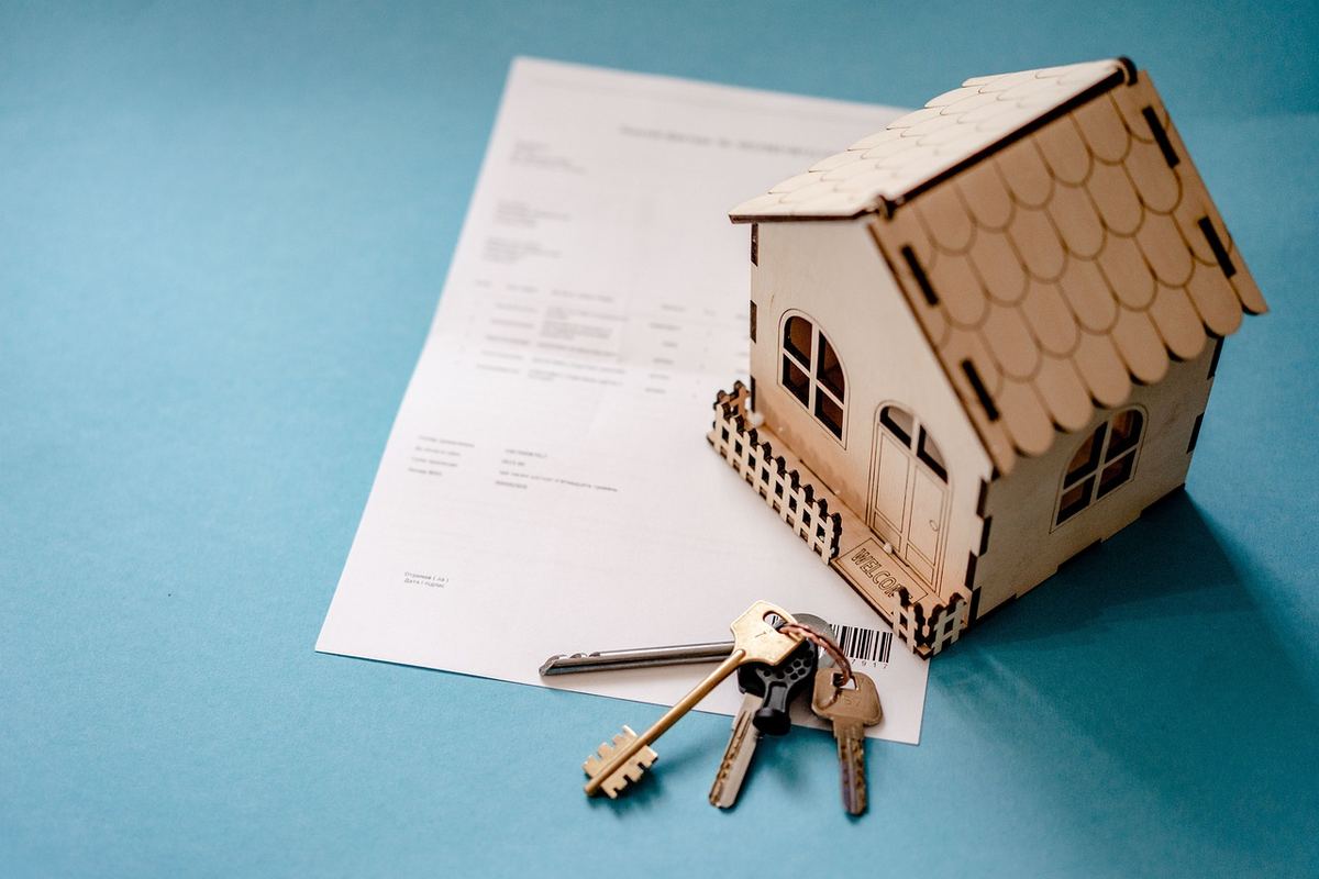 Une petite maison en bois, un document et des clés sur fond bleu