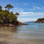 Plage rocheuse avec eau calme et végétation dense sous un ciel bleu