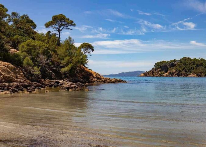 Plage rocheuse avec eau calme et végétation dense sous un ciel bleu