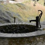 Un puits en pierre avec pompe manuelle, eau et colline herbeuse