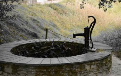 Un puits en pierre avec pompe manuelle, eau et colline herbeuse