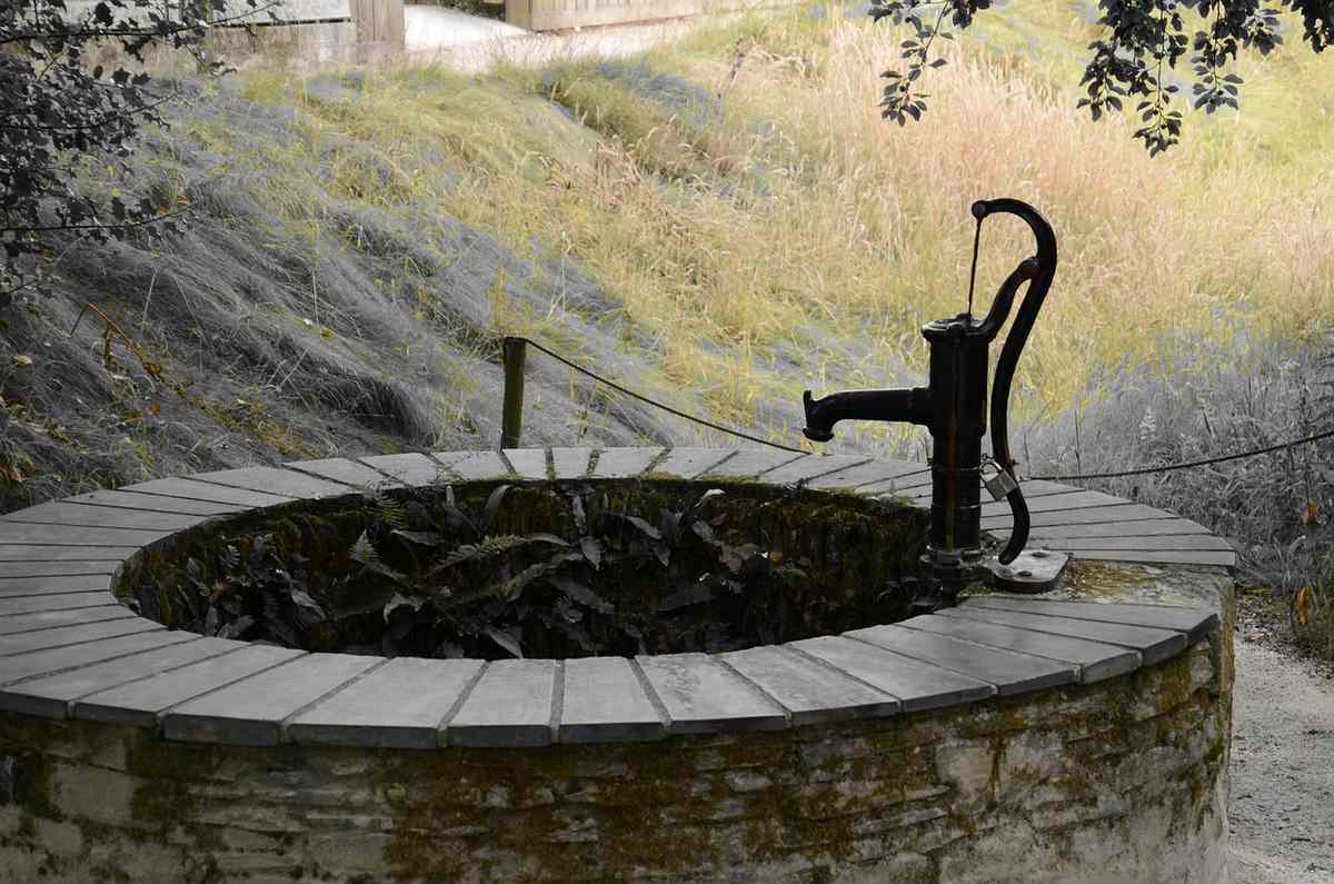 Un puits en pierre avec pompe manuelle, eau et colline herbeuse