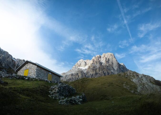 Refuge en pierre avec porte jaune au pied d'une montagne rocheuse, paysage alpin verdoyant