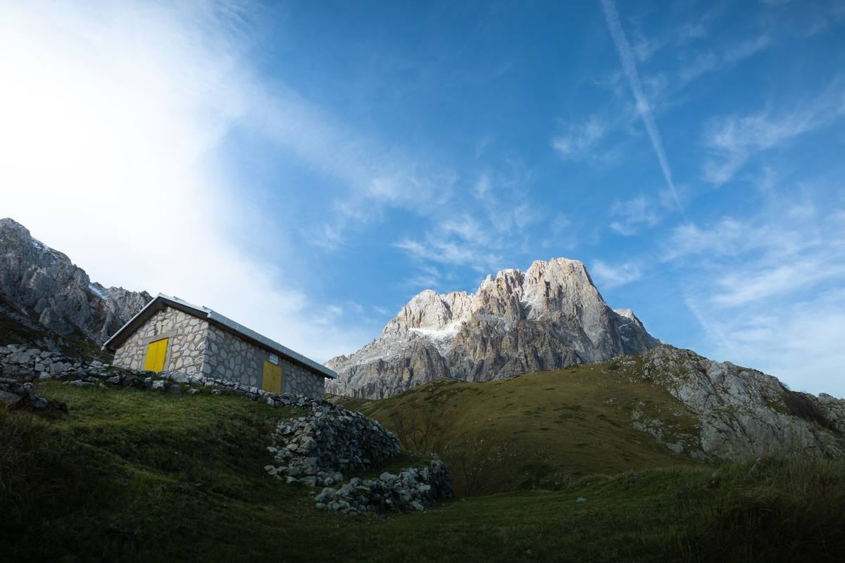 Refuge en pierre avec porte jaune au pied d'une montagne rocheuse, paysage alpin verdoyant