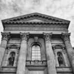 Vue d'une façade classique avec colonnes, statues et fronton sous ciel nuageux
