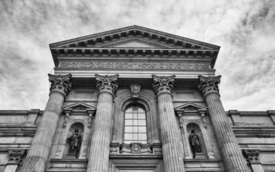 Vue d'une façade classique avec colonnes, statues et fronton sous ciel nuageux