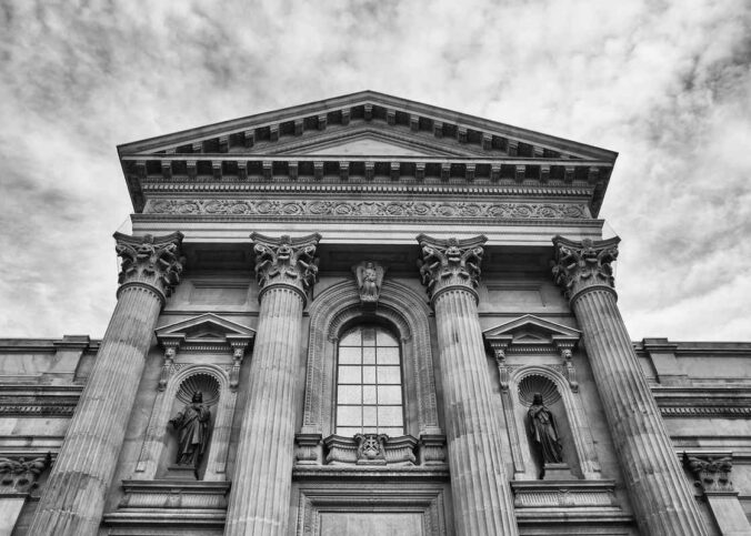 Vue d'une façade classique avec colonnes, statues et fronton sous ciel nuageux