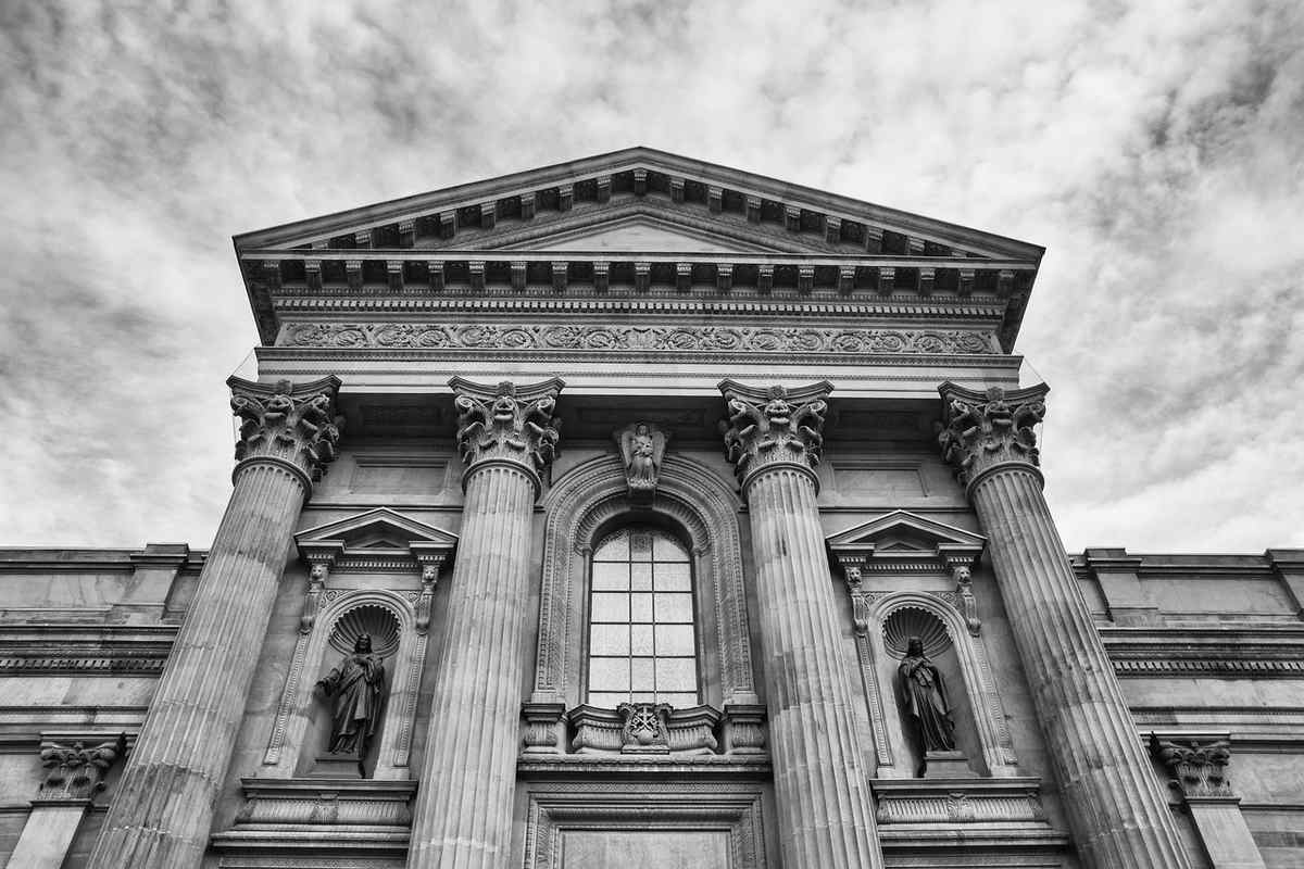 Vue d'une façade classique avec colonnes, statues et fronton sous ciel nuageux