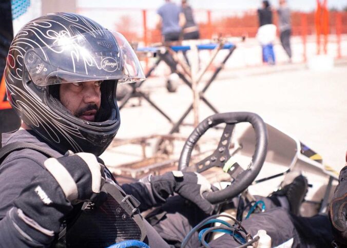 Un conducteur en casque noir pilote un kart sur circuit extérieur