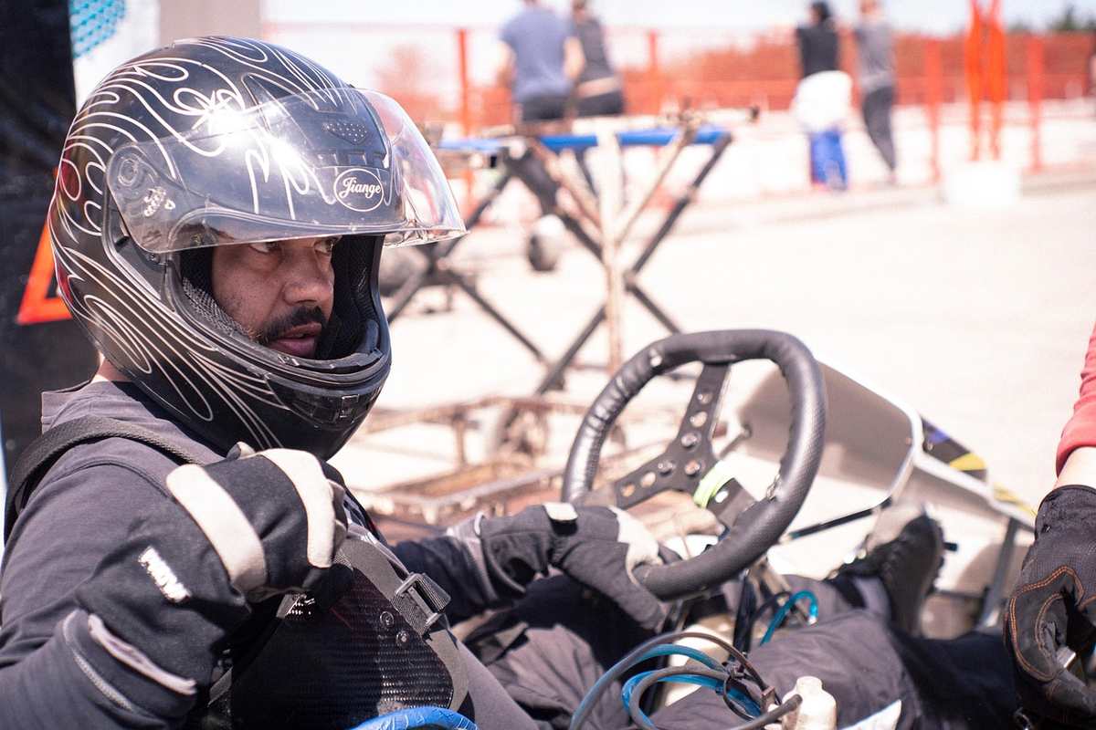 Un conducteur en casque noir pilote un kart sur circuit extérieur